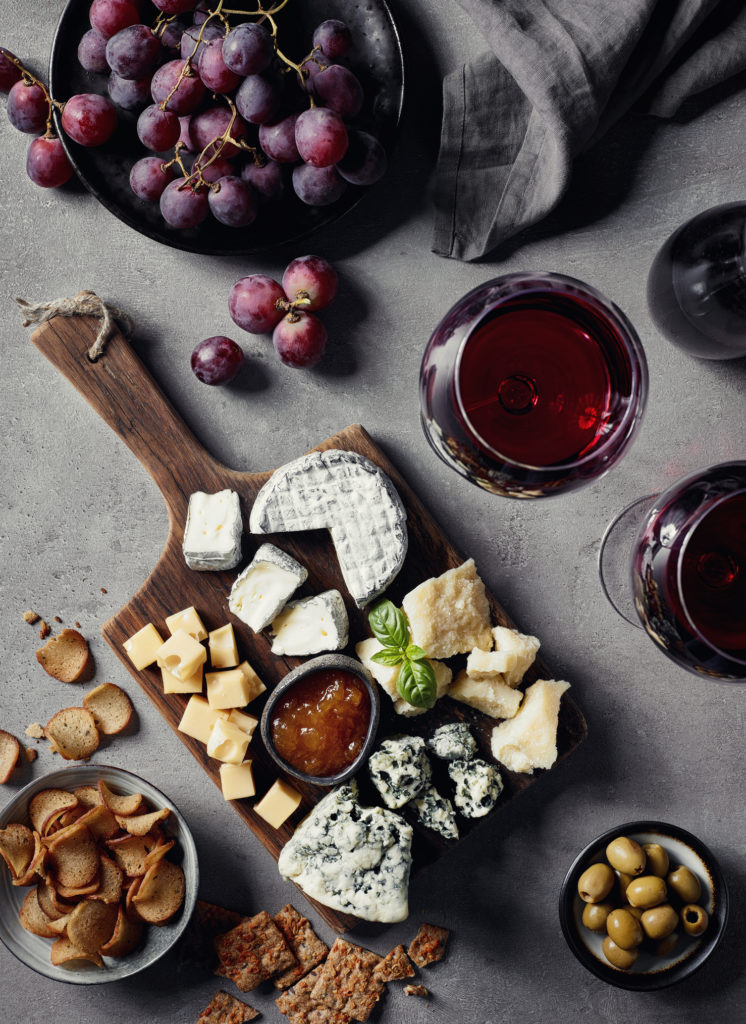 Cheese plate served with red wine, olives, grapes, jam and bread snacks on gray marble background. Top view.
